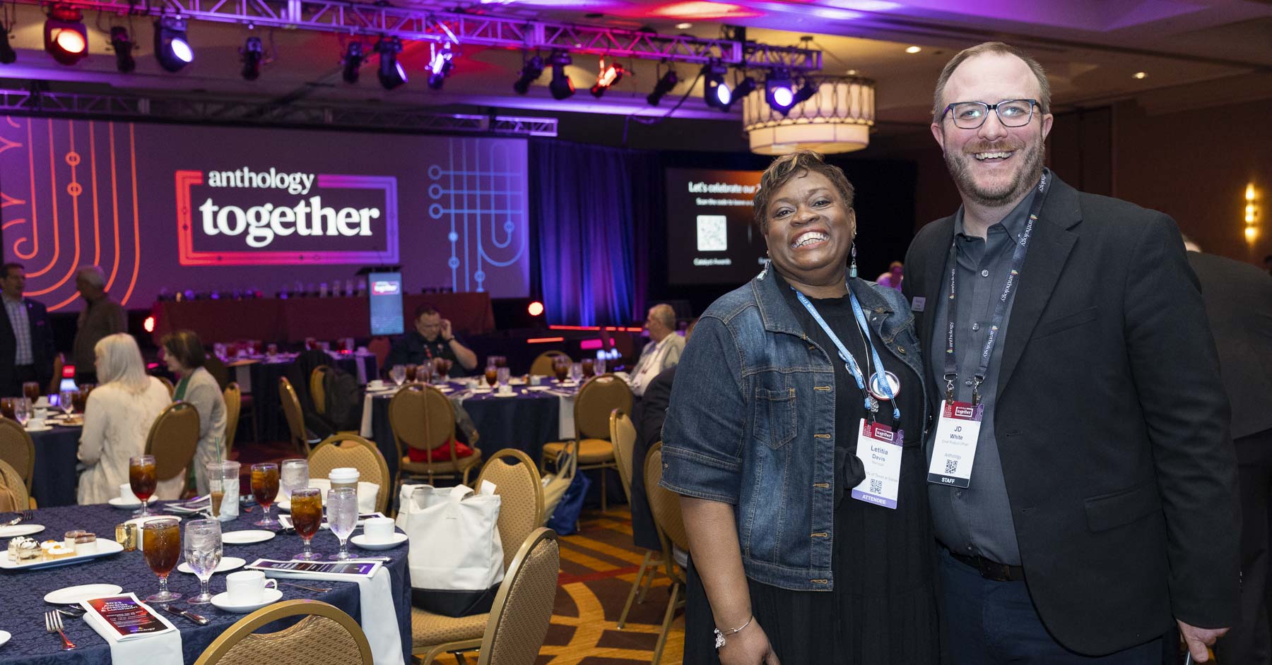 Two attendees smiling by the Anthology Together stage