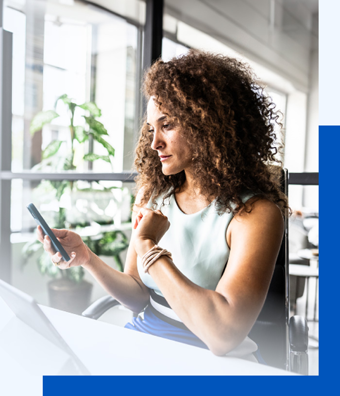 Photo of a woman sitting in front of a laptop and looking at something on her phone