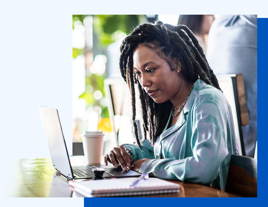 Photo of a woman working at a laptop with a notebook and coffee cup on each side