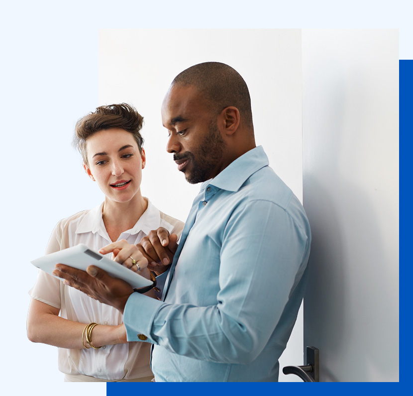 Photo of two people standing up against a wall looking at something on a tablet