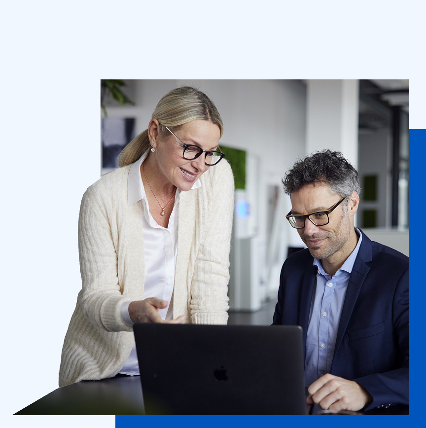 Photo of a woman showing something on a laptop to a man sitting in front of the computer