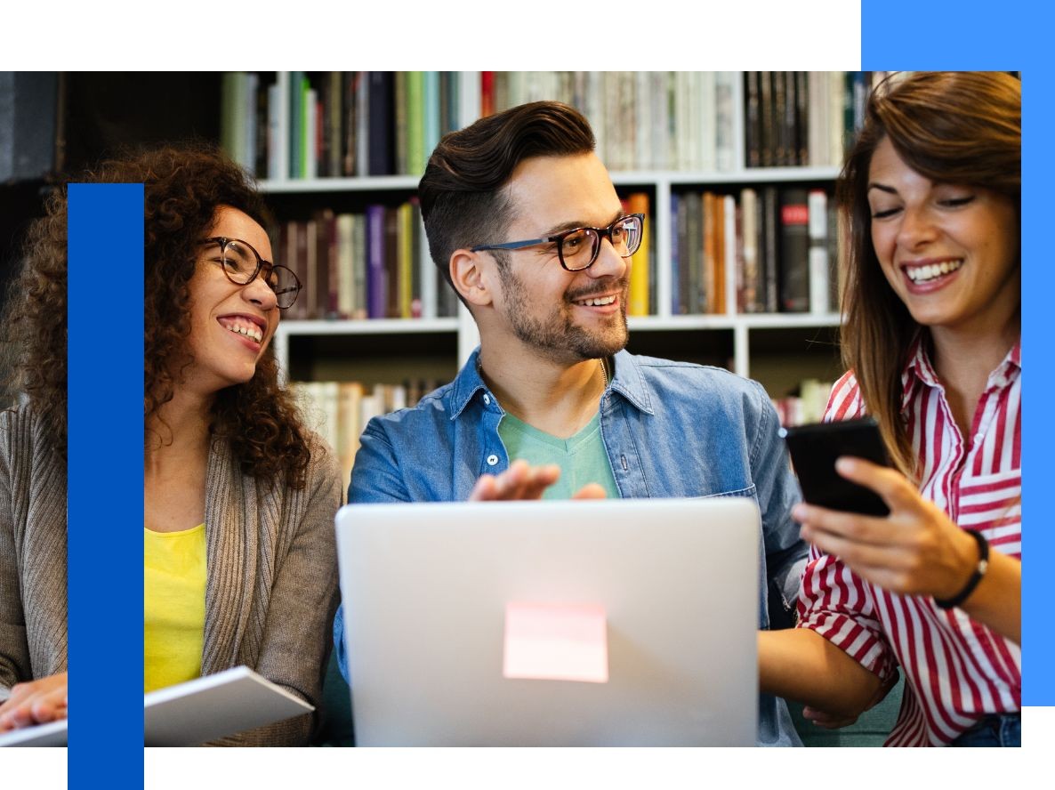 Photo of three people working in a library in front of a laptop