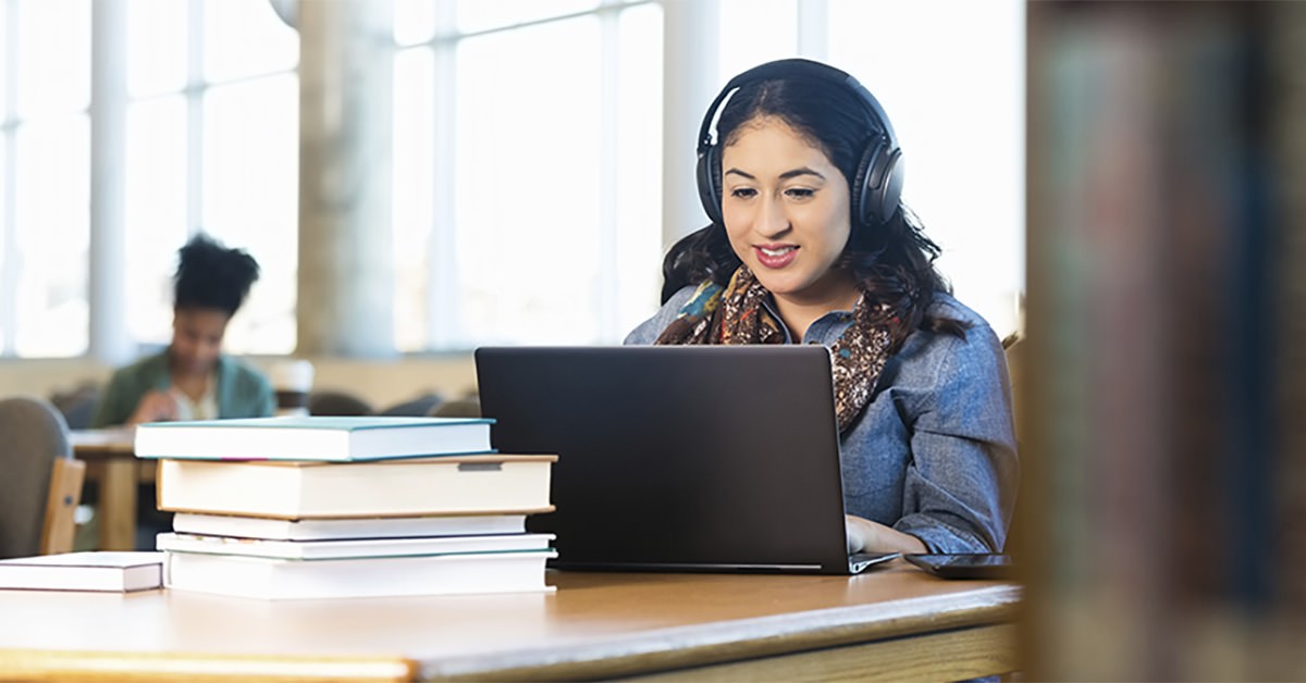 Photo of a person wearing headphones working at a laptop in a library