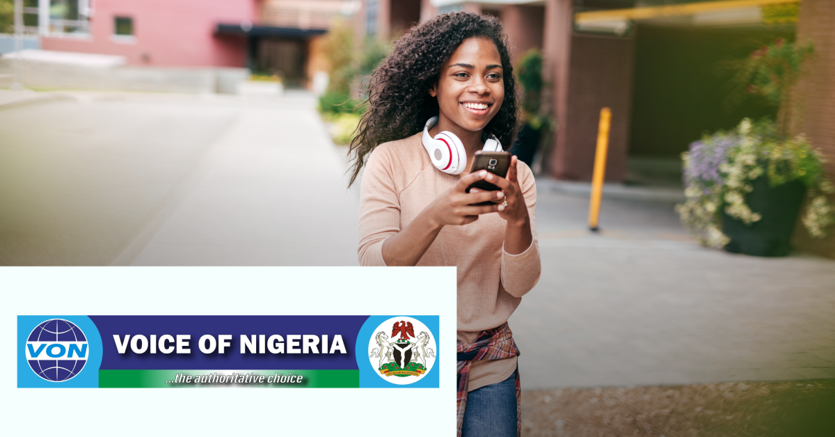 Image of a woman walking while holding her mobile phone on her hands. On the lower left corner of the graphic is placed the Voice Of Nigeria logo. 