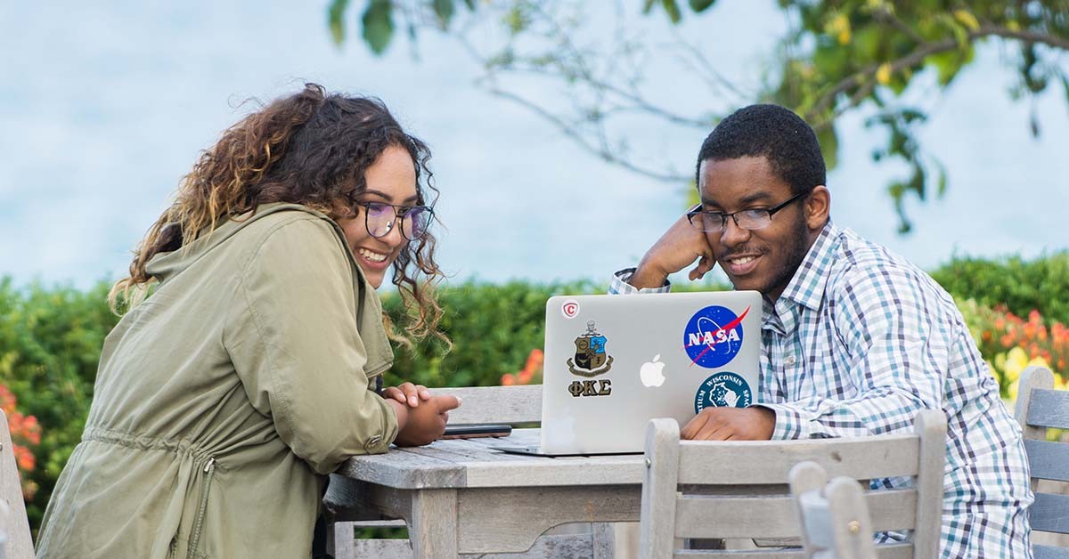 Photo of two students collaborating at a laptop outside