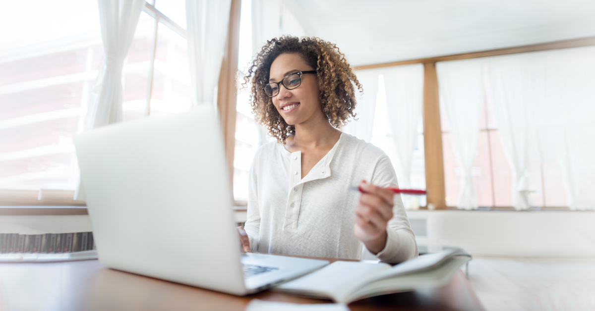 Photo of a woman working at a laptop and taking notes in a notebook