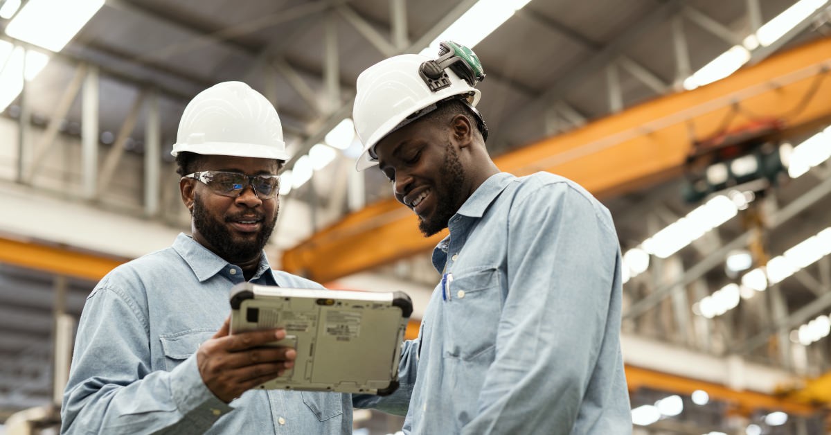Two people wearing hard hats on the floor of a manufacturing plant