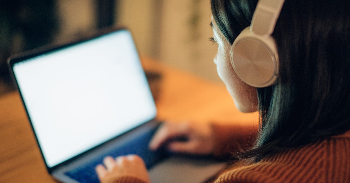 Photo of a woman working at her laptop with headphones on