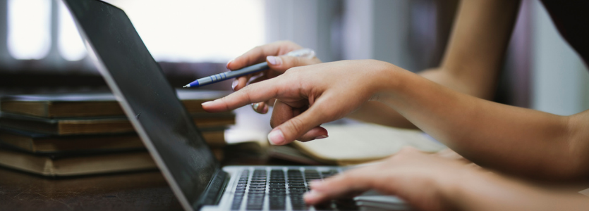 Photo of the hands of two people pointing at a laptop they are working at