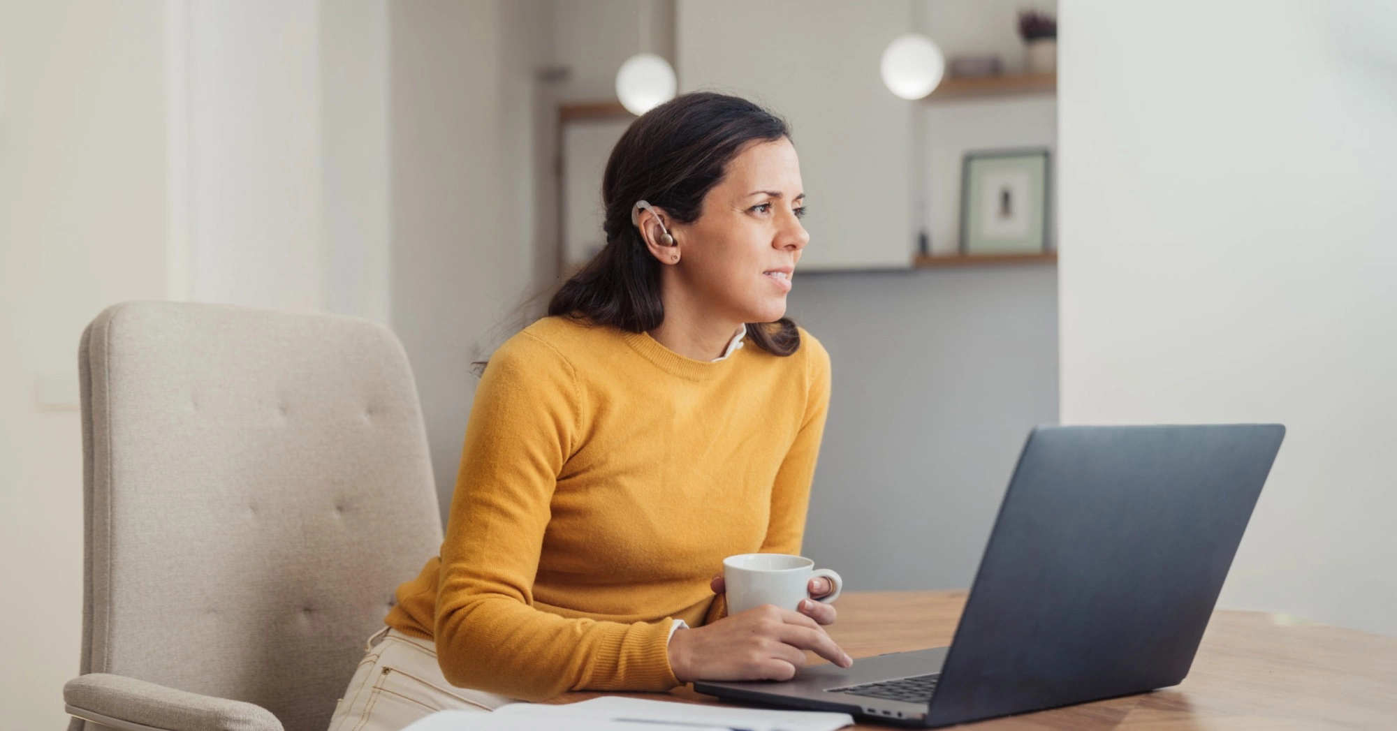 Photo of a person with a hearing aid sitting at their desk with a laptop open